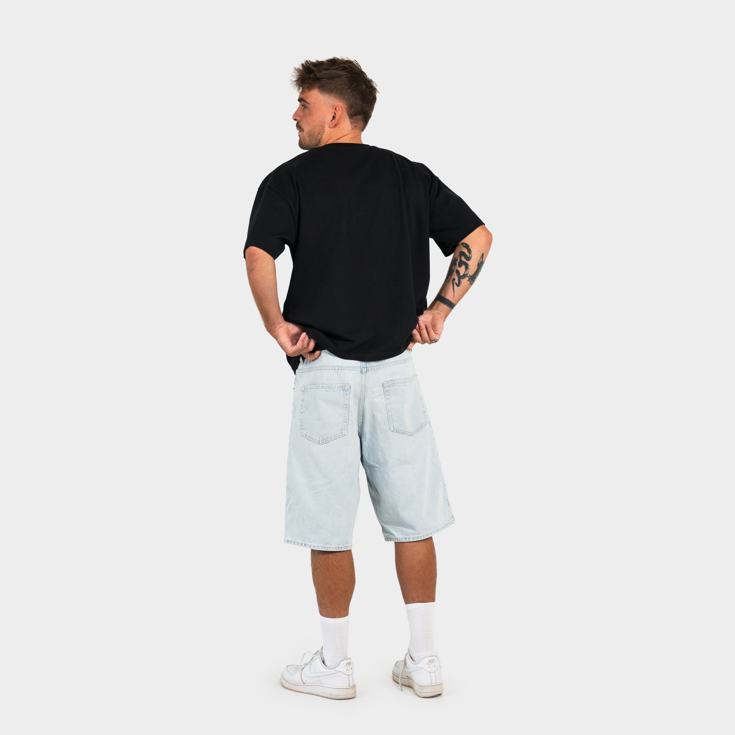 Person wearing a black 'taze studios' t-shirt and light blue shorts on a white background