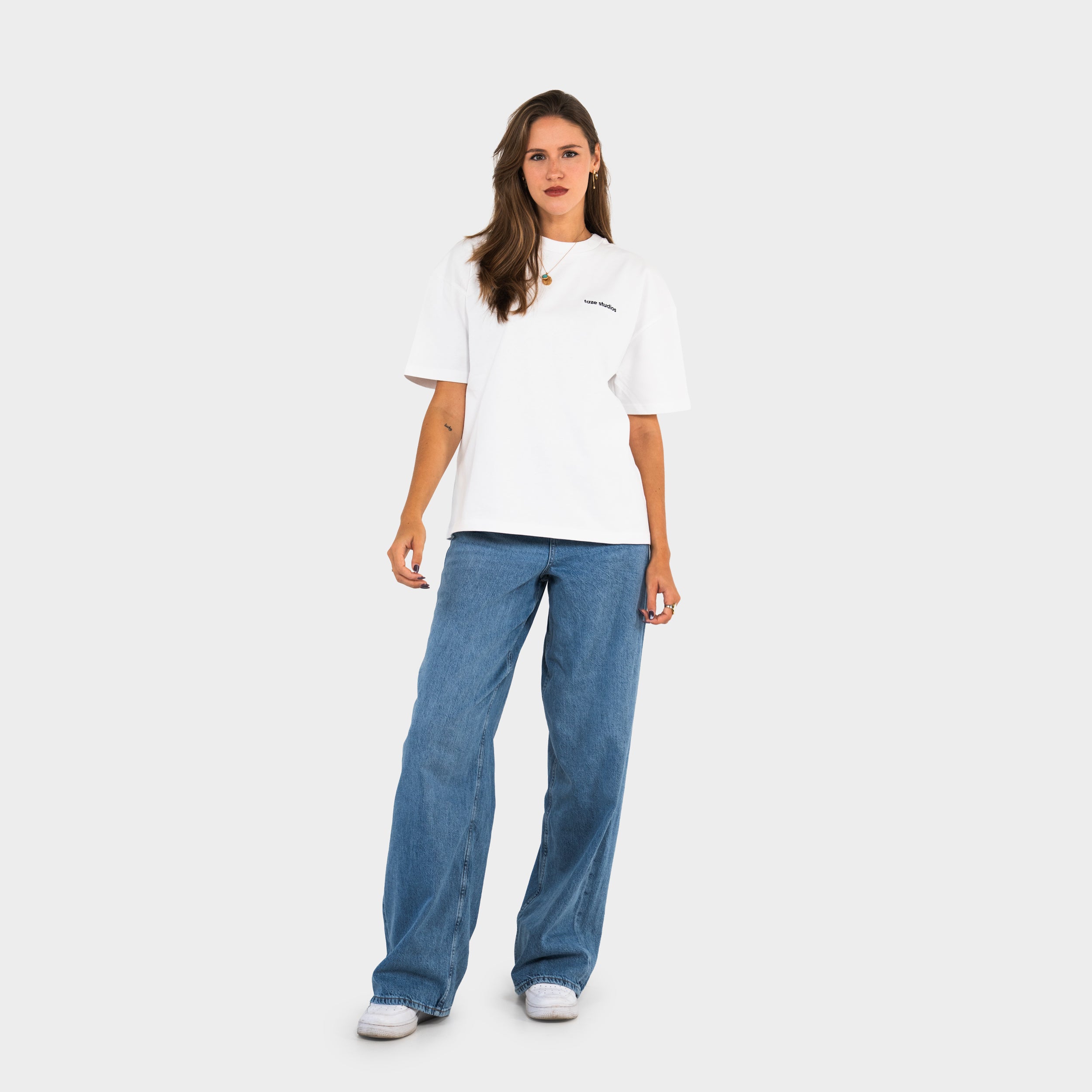 Woman wearing a white 'taze studios' t-shirt and blue jeans on a white background