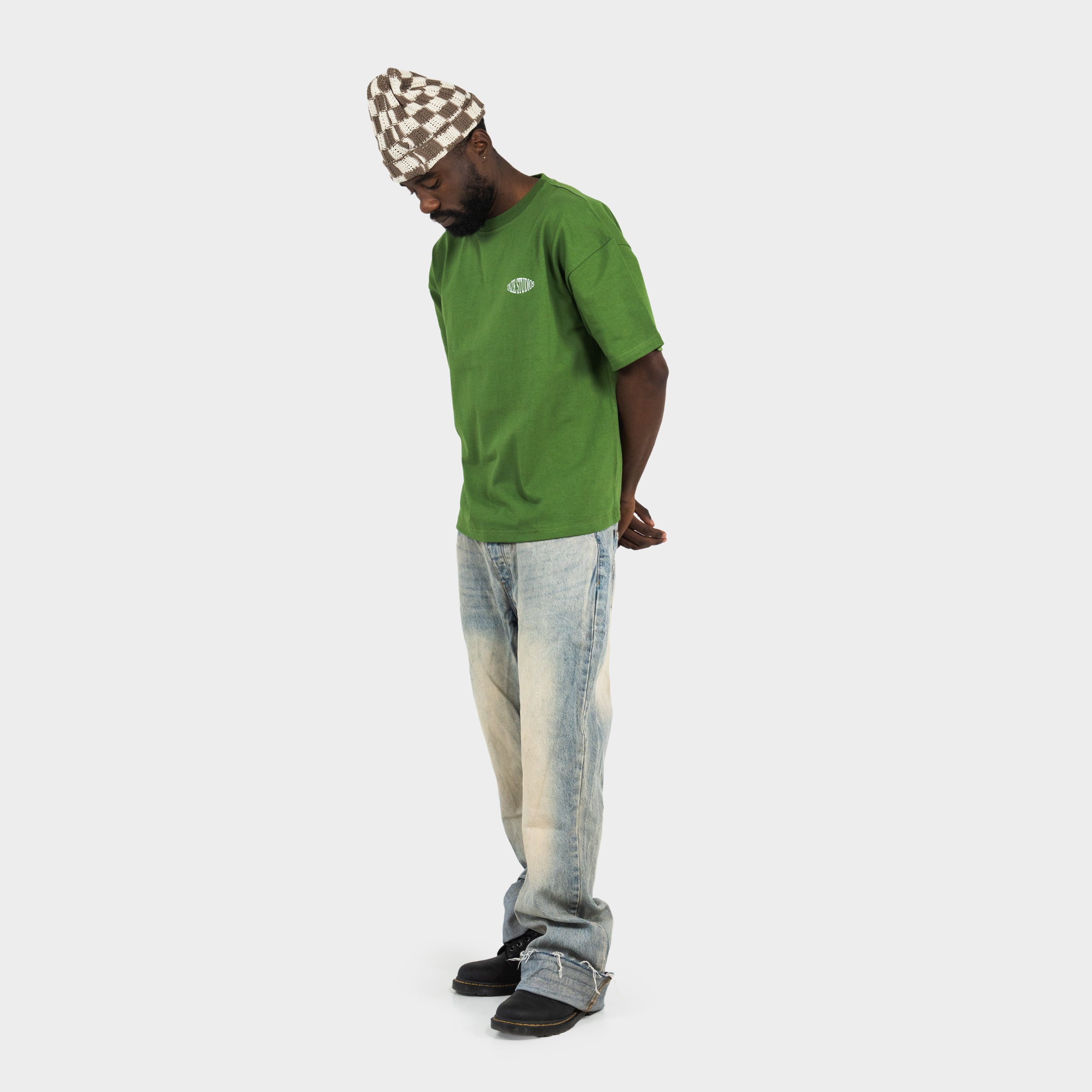 Male wearing a green boxy t-shirt with 'taze studios' logo on the front, standing against a white background.