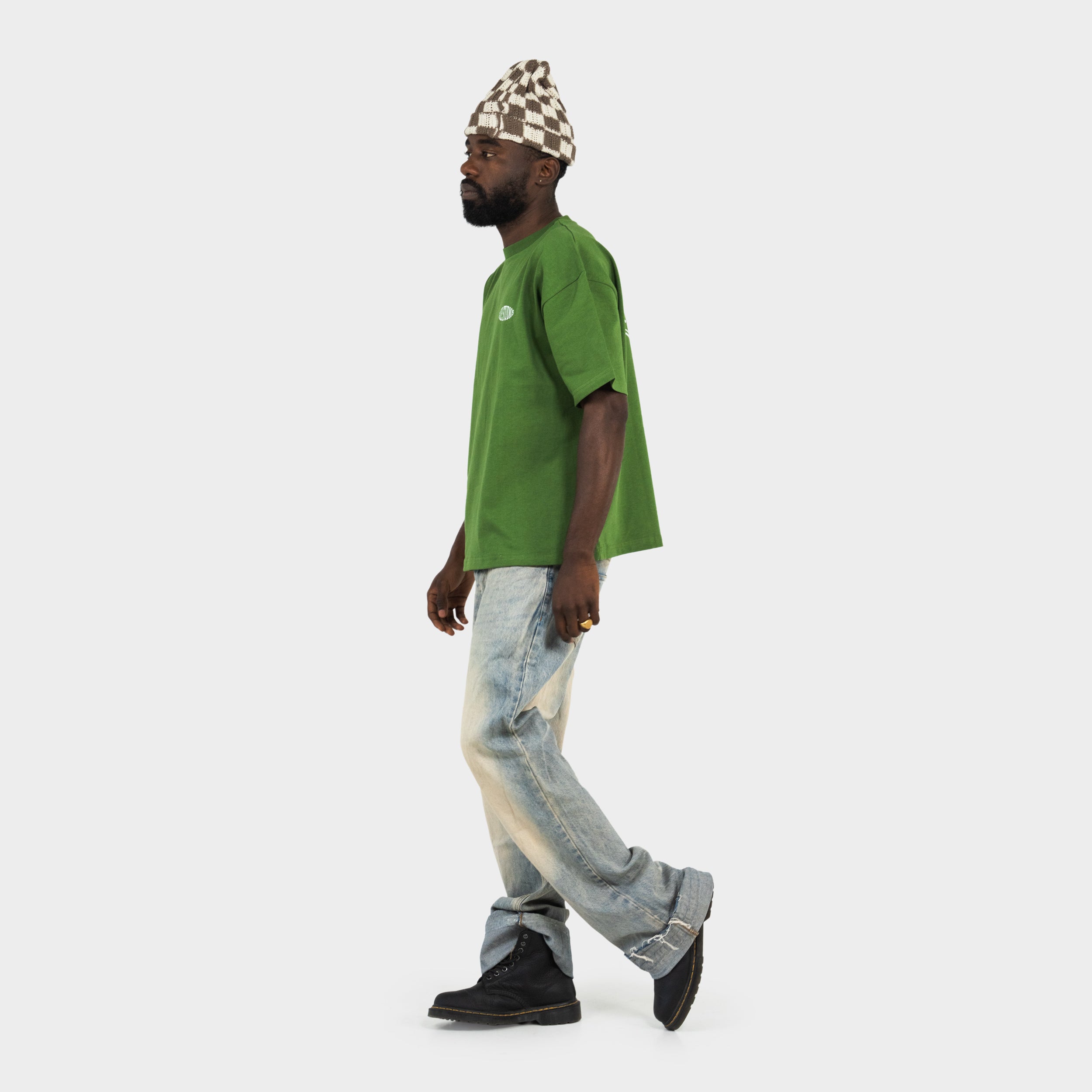 Man wearing a green 'taze studios' t-shirt, checkered beanie, and distressed jeans on a white background.