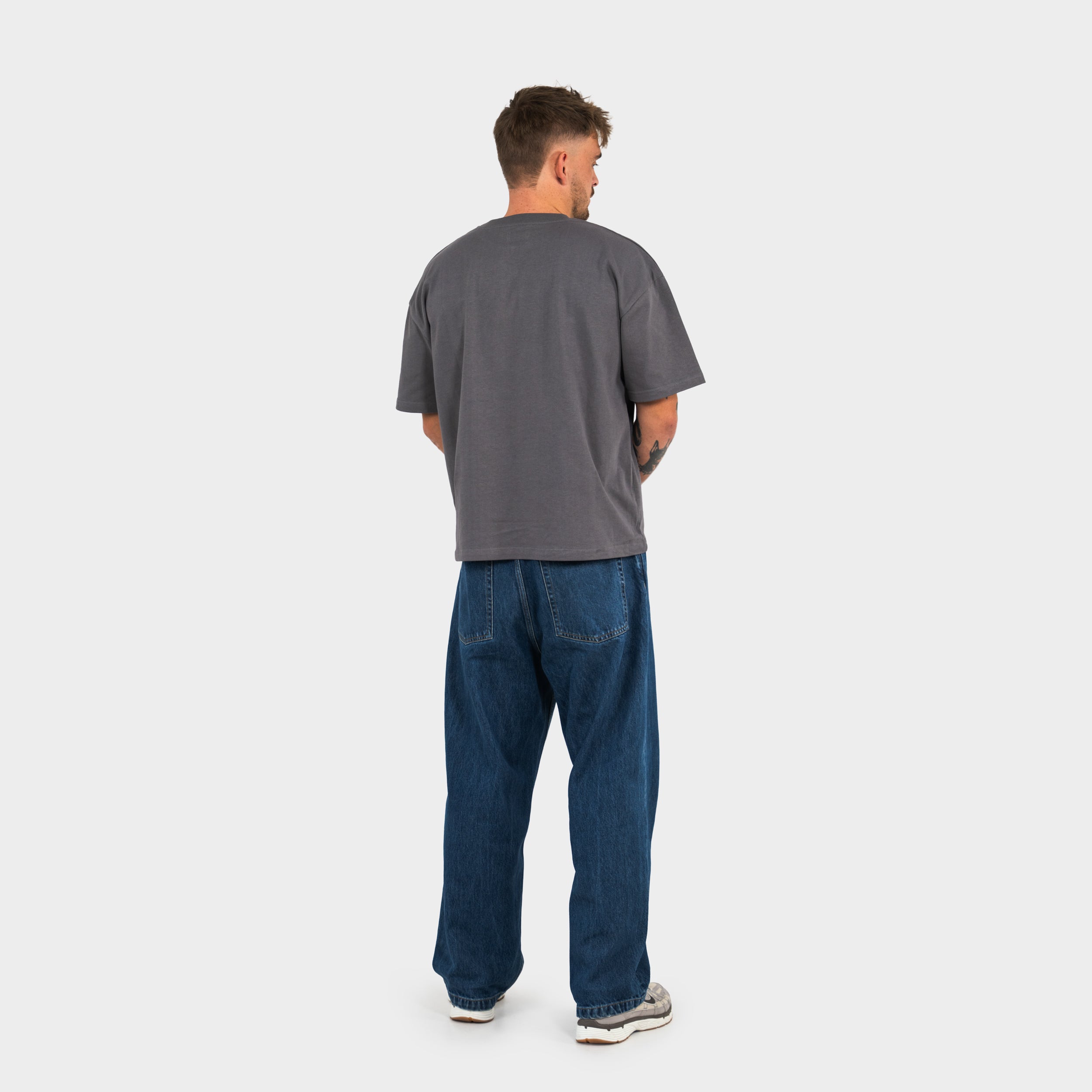 Man wearing a gray 'taze studios' t-shirt and blue jeans on a white background