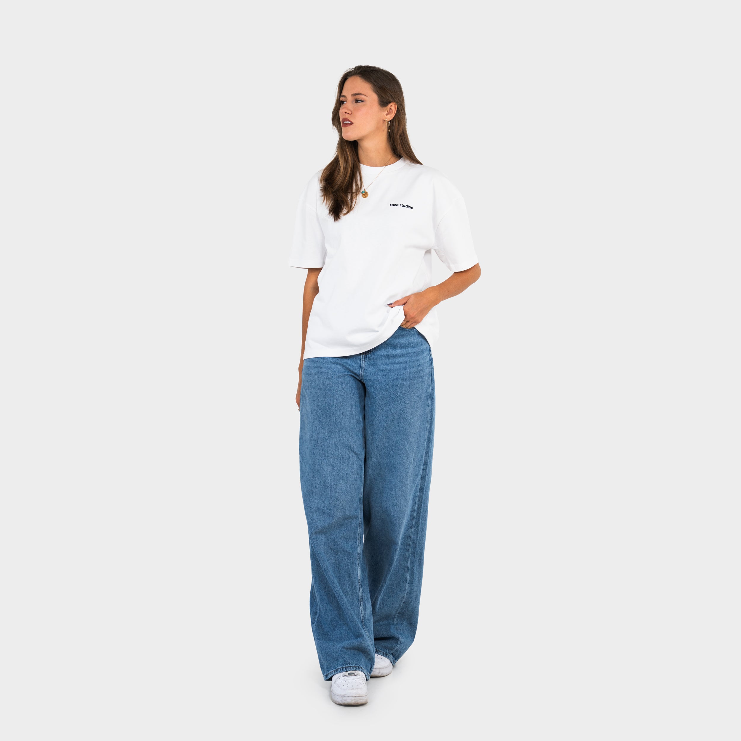 Woman wearing a white 'taze studios' t-shirt and blue jeans on a white background