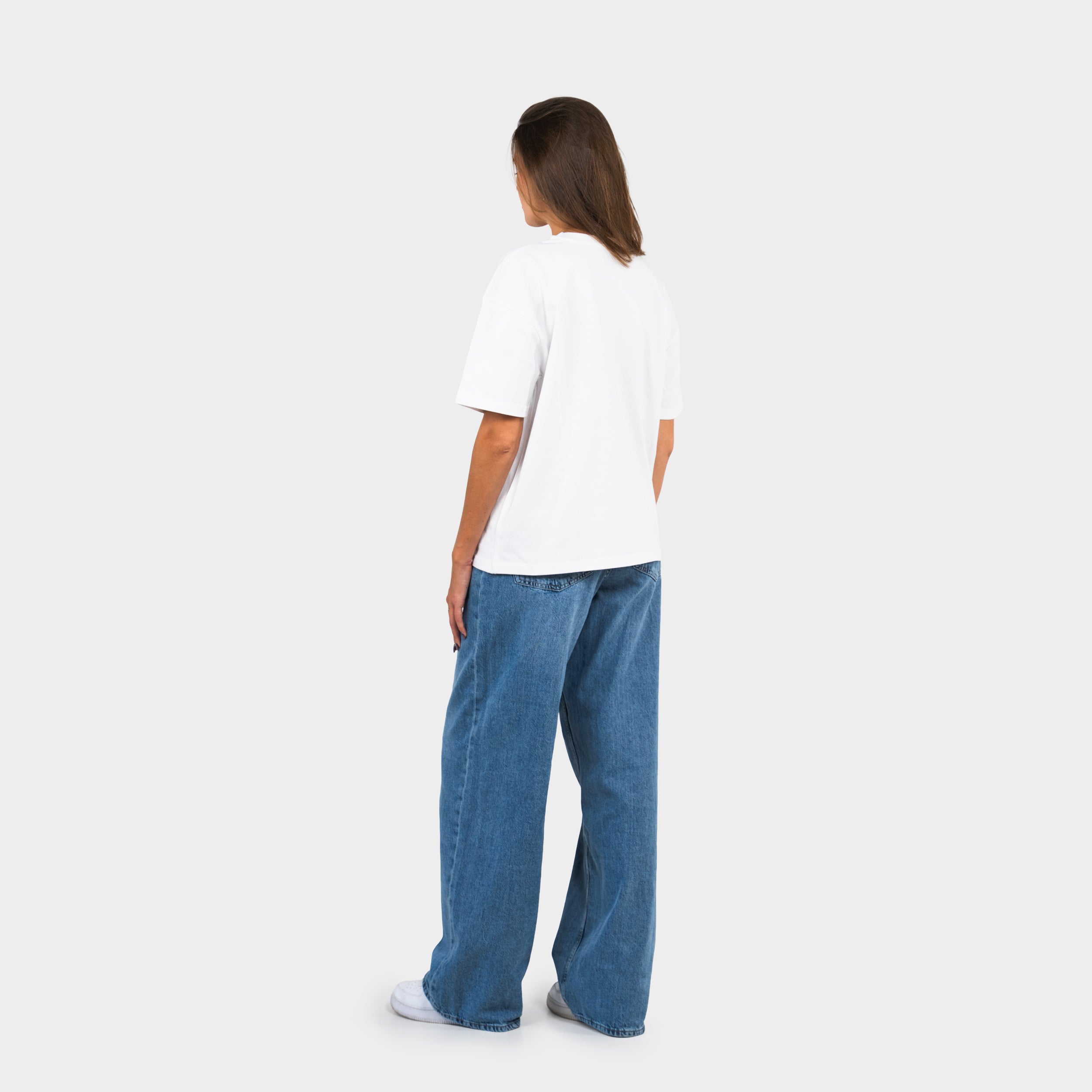 Woman wearing a white 'taze studios' t-shirt and blue jeans on a white background