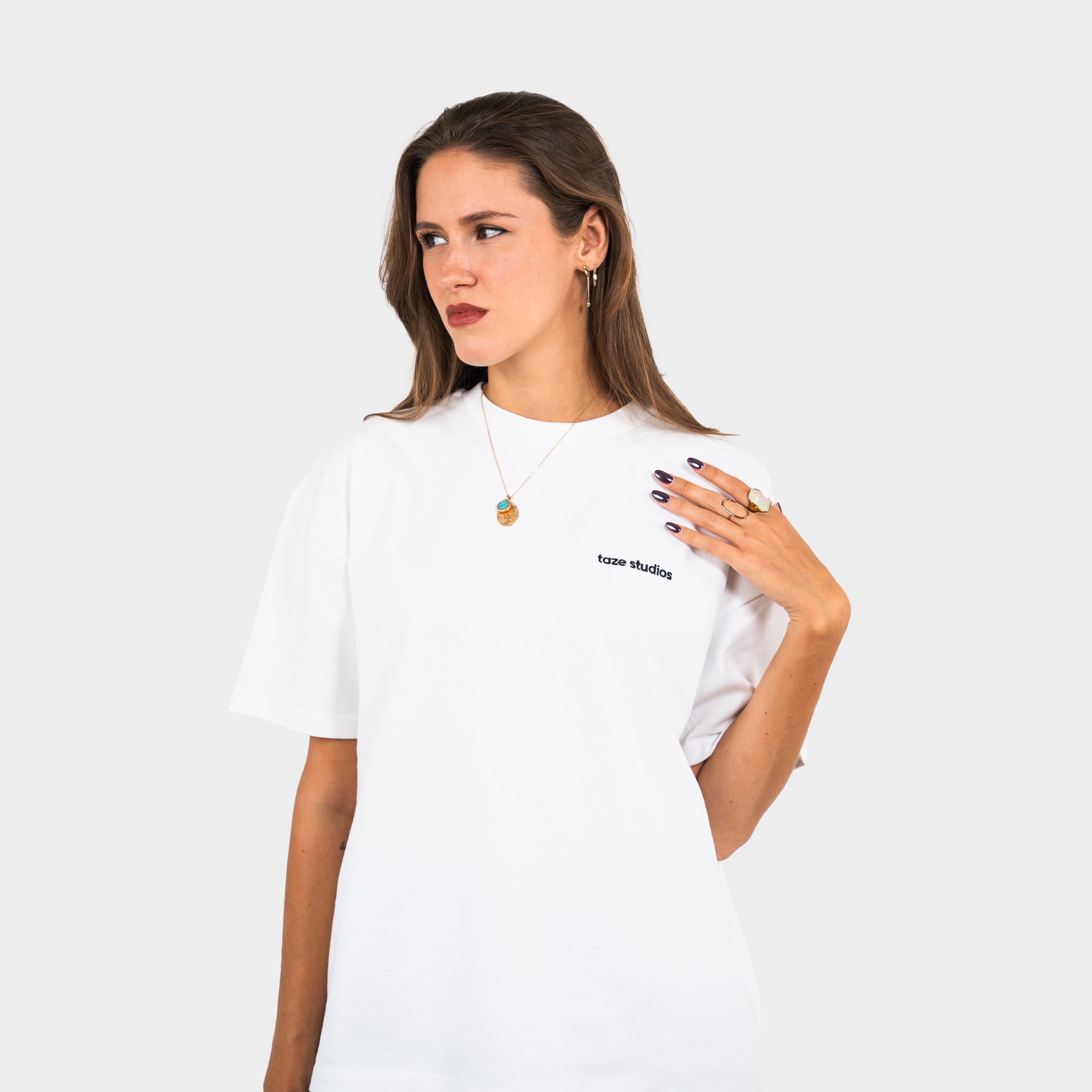 Woman wearing a white 'taze studios' t-shirt with logo, on a white background