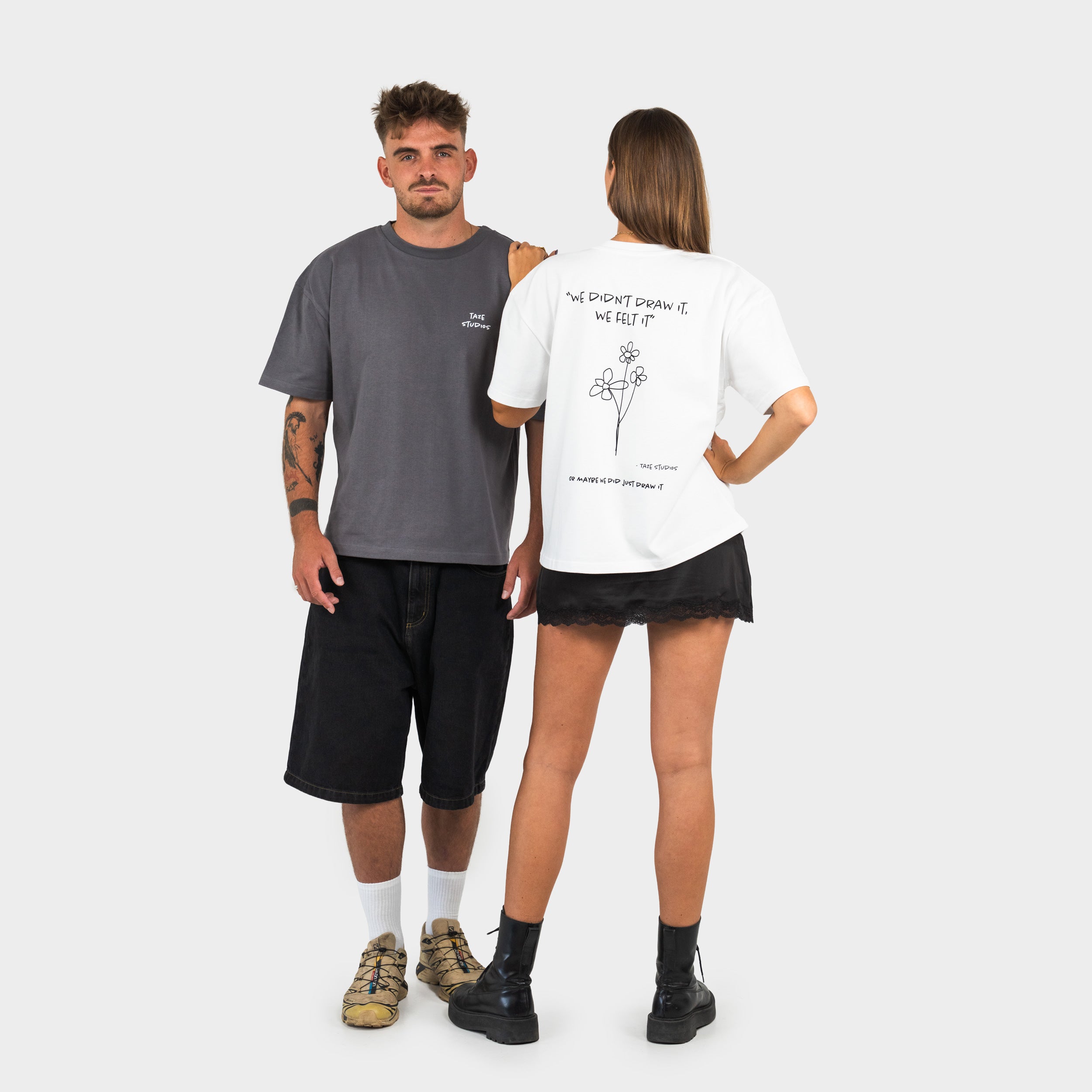 Two people wearing t-shirts with 'taze studios' logo on the front and artwork on the back, standing against a plain background