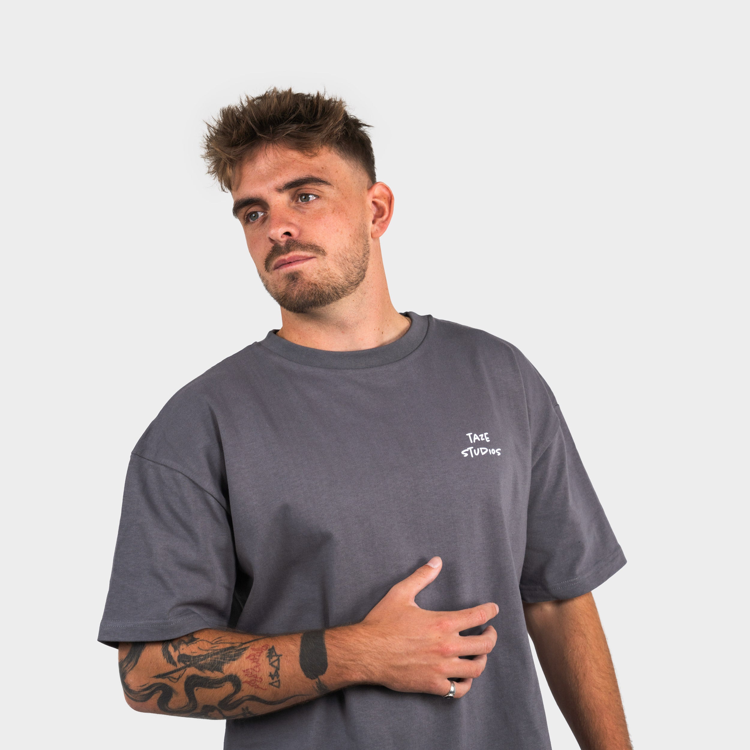 Man wearing a gray t-shirt with 'taze studios' logo on a plain background
