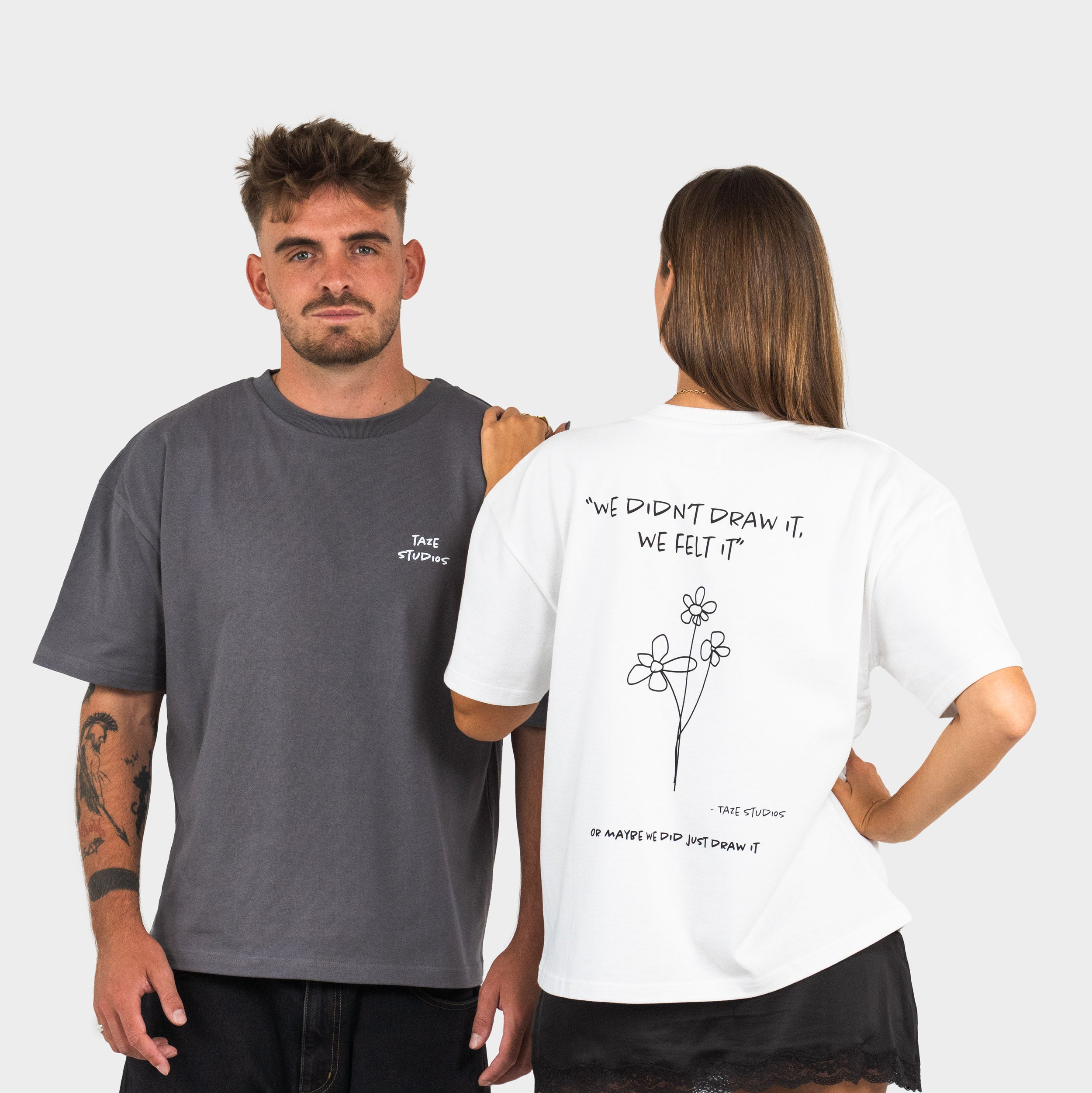 Two people wearing t-shirts with 'taze studios' logo on the front and artwork on the back, standing against a plain background