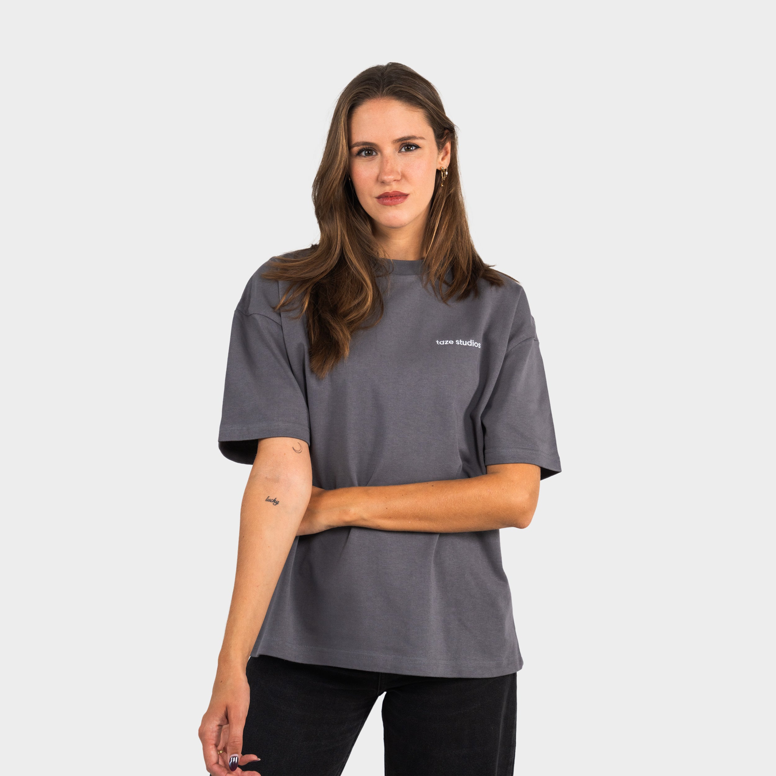 Female wearing a grey T-shirt with the 'taze studios' logo on the chest, standing against a white background.